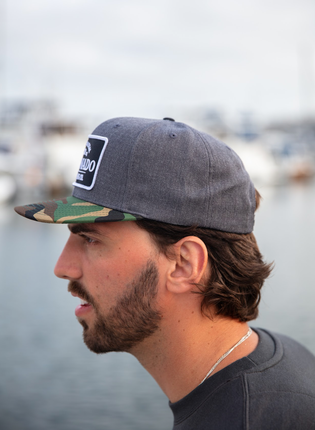 Man wearing a Coronado Brewing Co. hat with a blurred background of water and boats