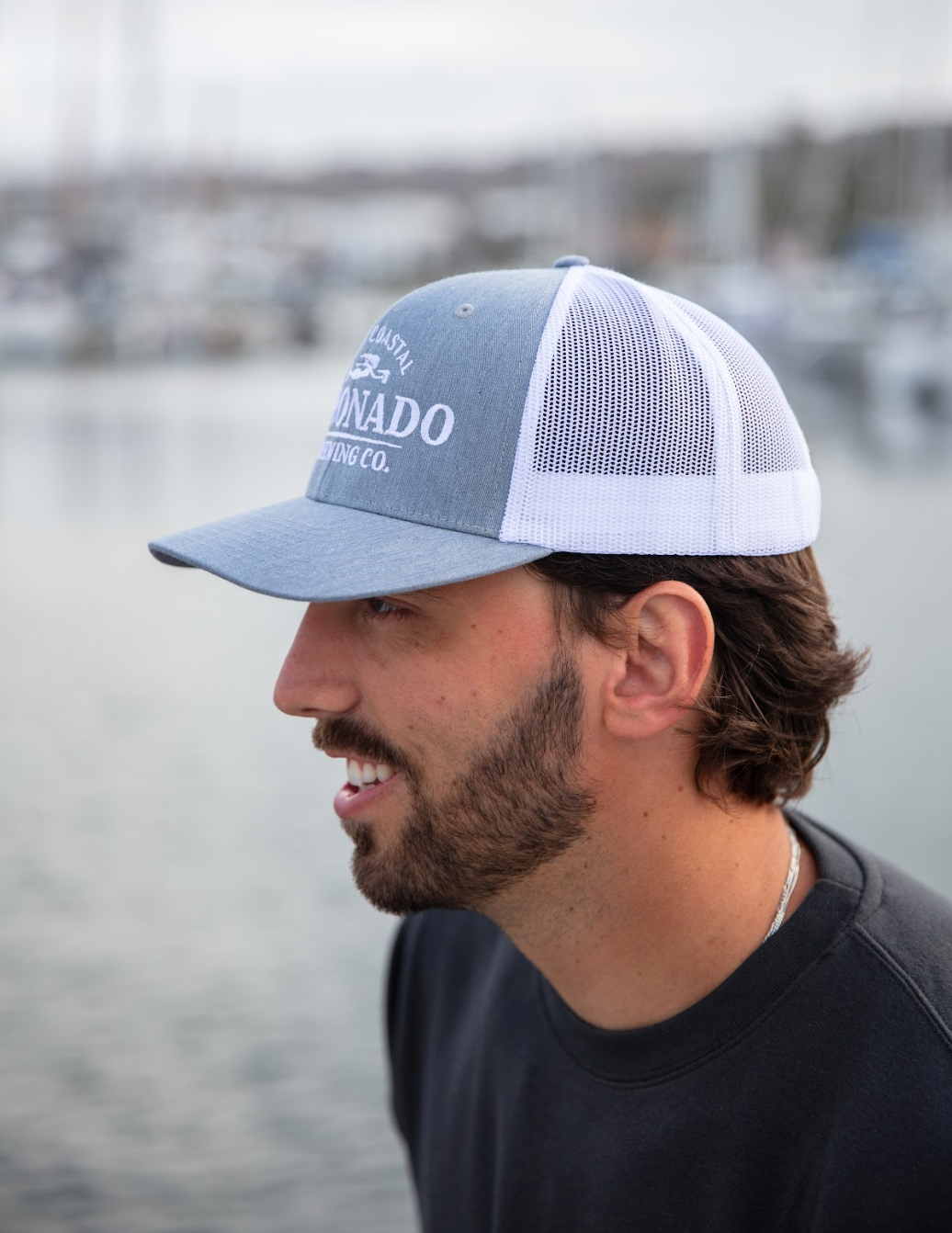Man wearing a gray and white Coronado Brewing Co. hat, standing by water.