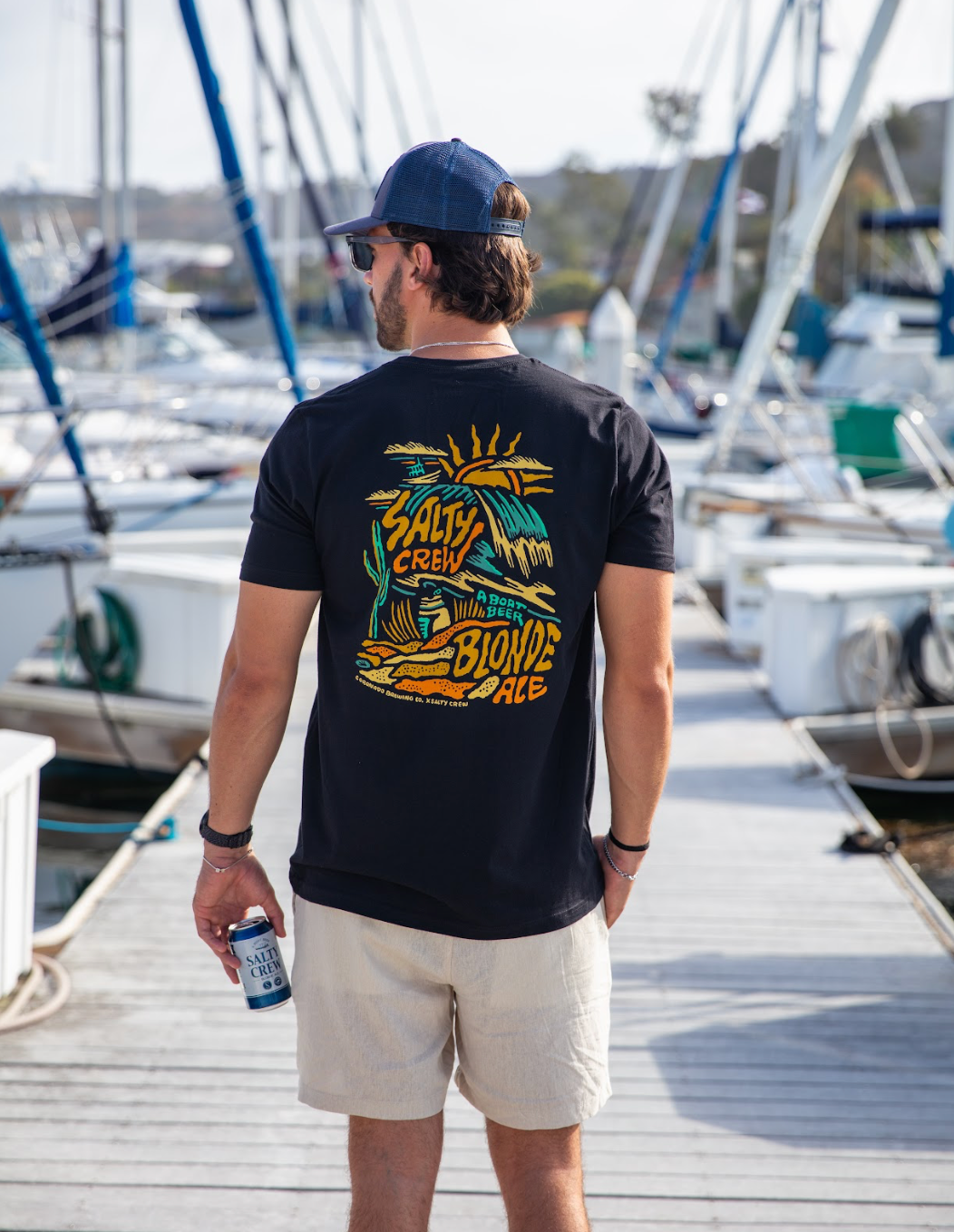 Man wearing a black t-shirt with a graphic design, standing on a dock with boats in the background.