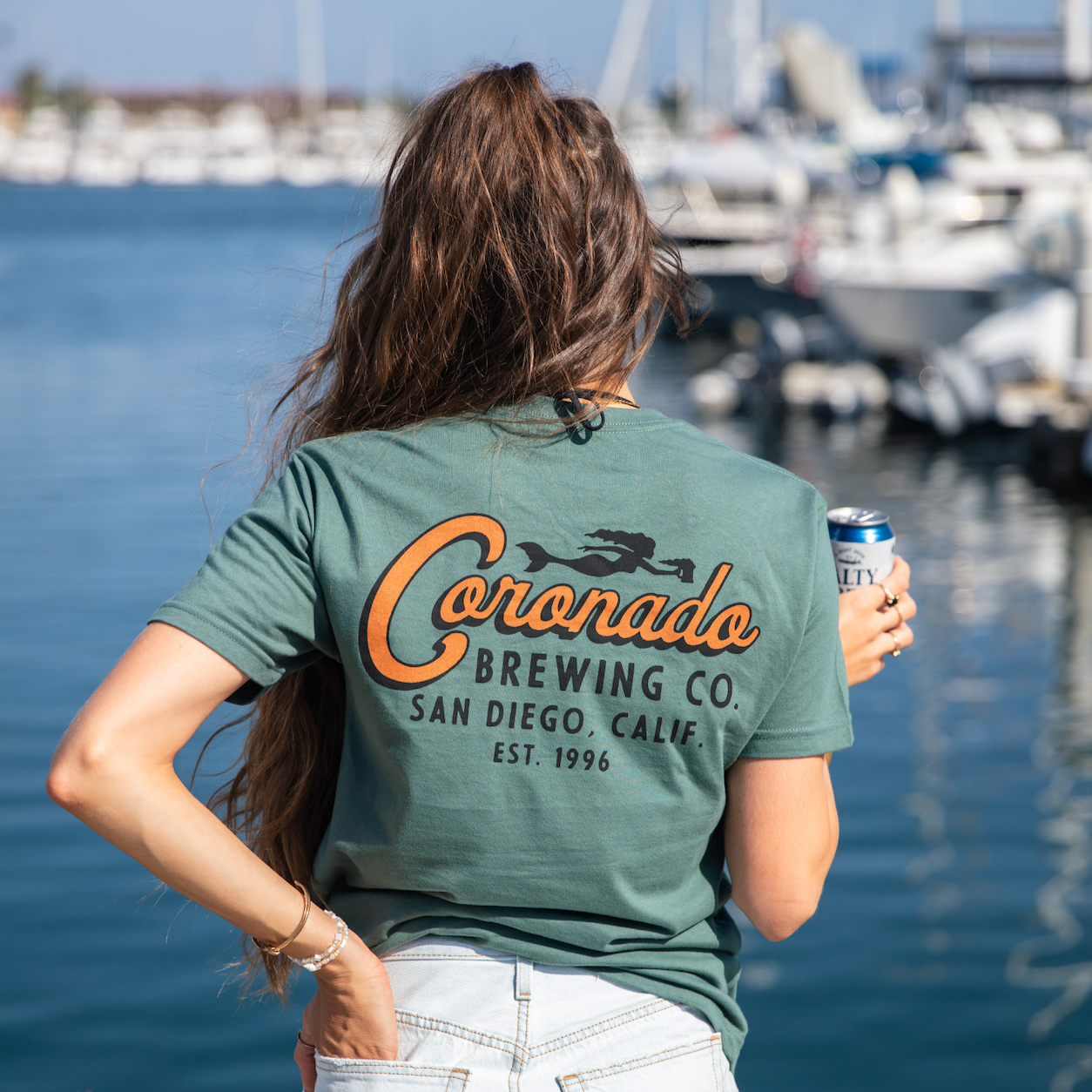 Women wearing a green 'Coronado Brewing Co' t-shirt by a marina.