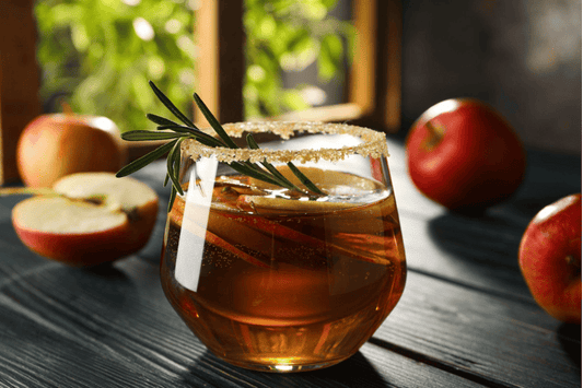 A glass of cider on a dark wooden table surrounded by apples