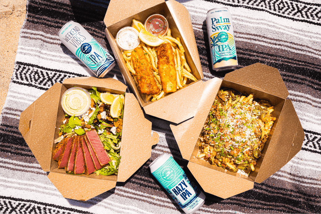 Assorted Coronado beers and boxed meals on a beach blanket, showing low and high IBU options side by side