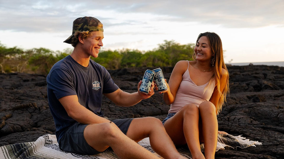Two friends toasting Big Weekend Double IPA on rocky shoreline at sunset, highlighting bold IPA side in pale ale vs IPA.