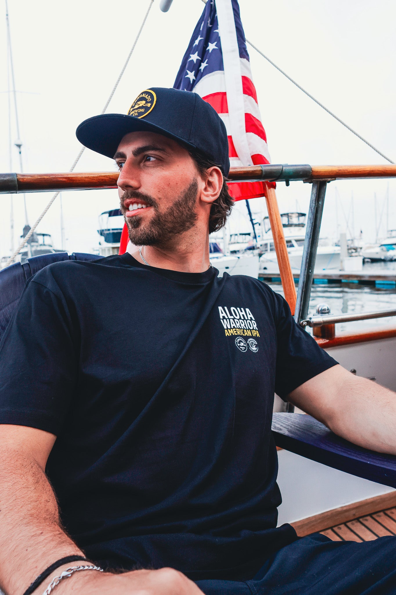 A man wearing a Aloha Warrior t-shirt with a logo on a boat with an American flag in the background