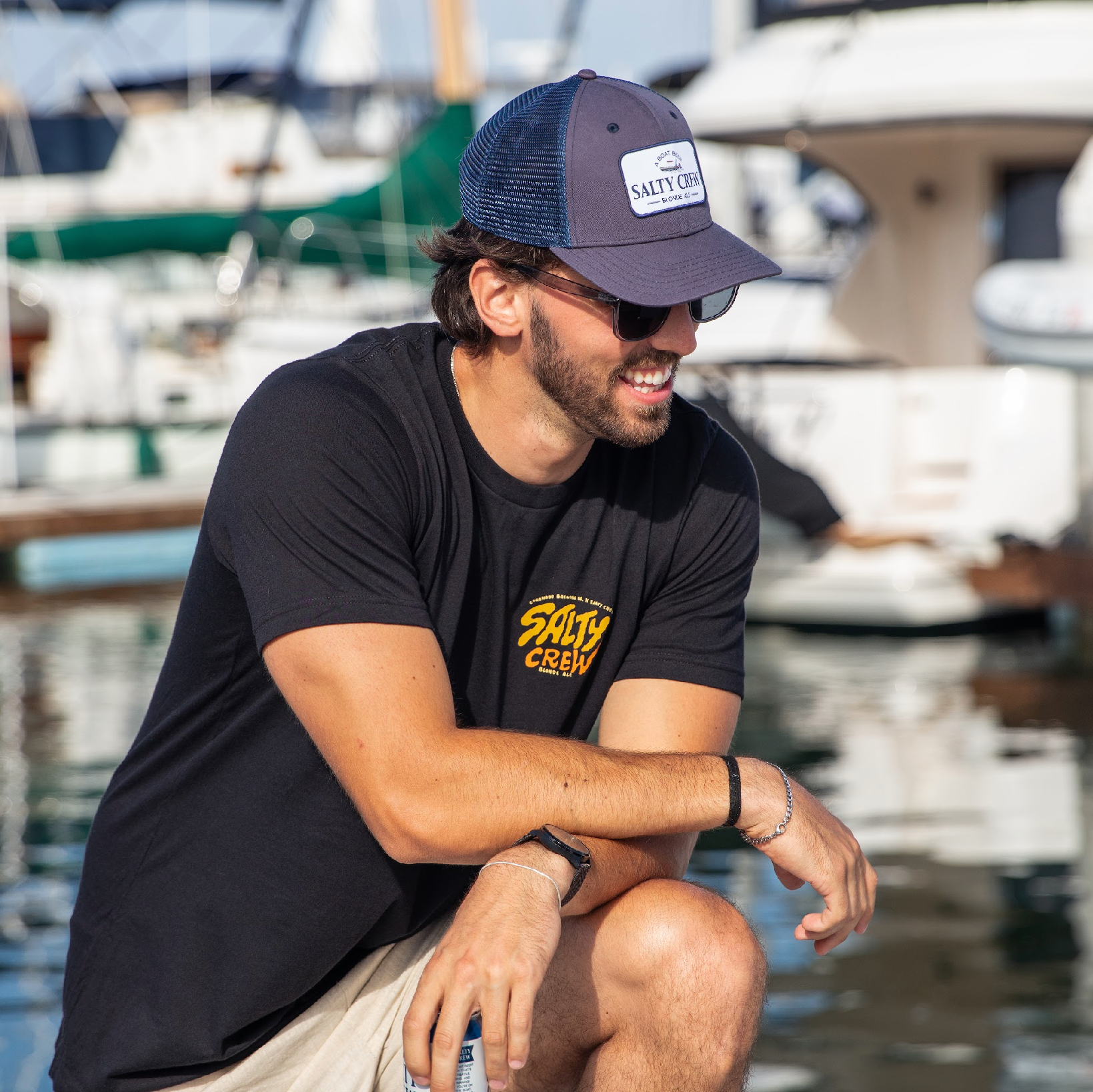 Man wearing a Salty Crew cap and t-shirt sitting by a marina.