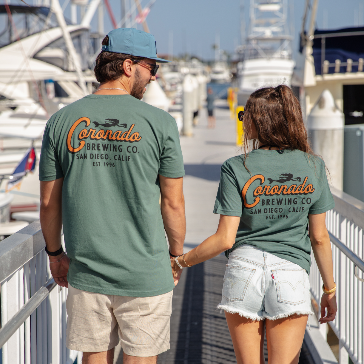 Two people wearing Coronado Brewing Co. t-shirts at a marina.