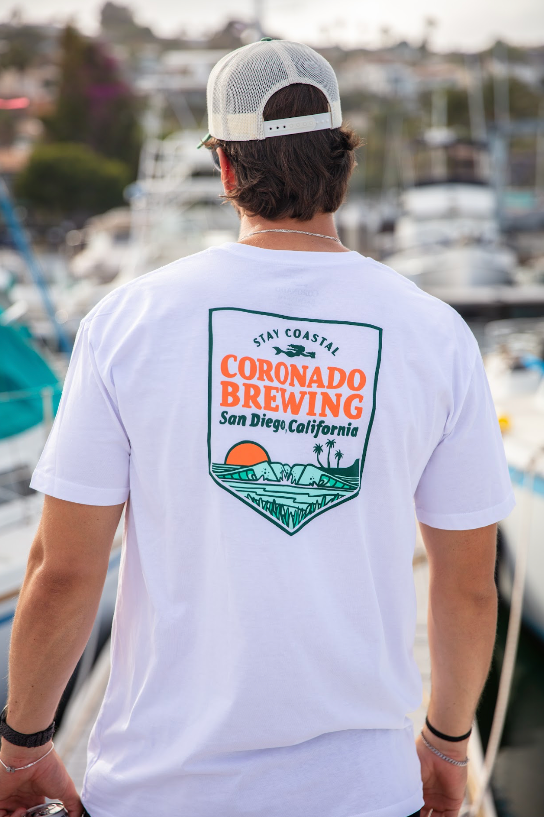 Person wearing a white t-shirt with Coronado Brewing logo at a marina.