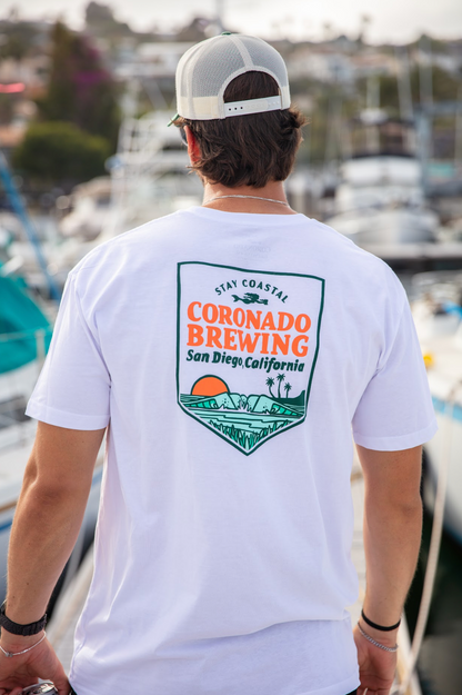 Person wearing a white t-shirt with Coronado Brewing logo at a marina.