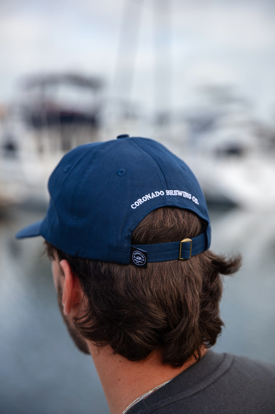 Person wearing a blue cap with 'Coronado Brewing Co' on it, blurred background