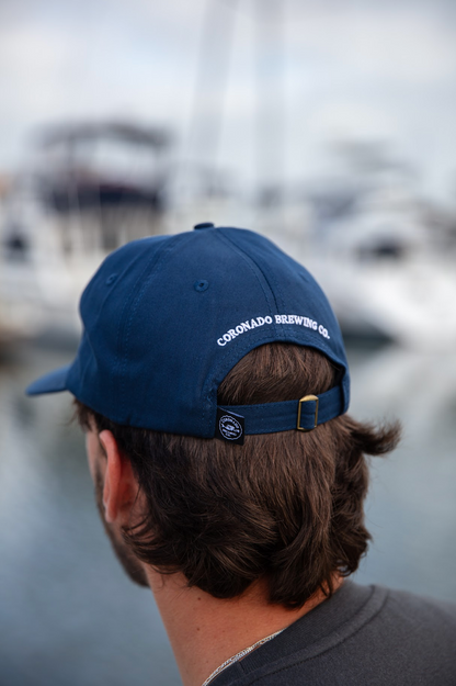 Person wearing a blue cap with 'Coronado Brewing Co' on it, blurred background