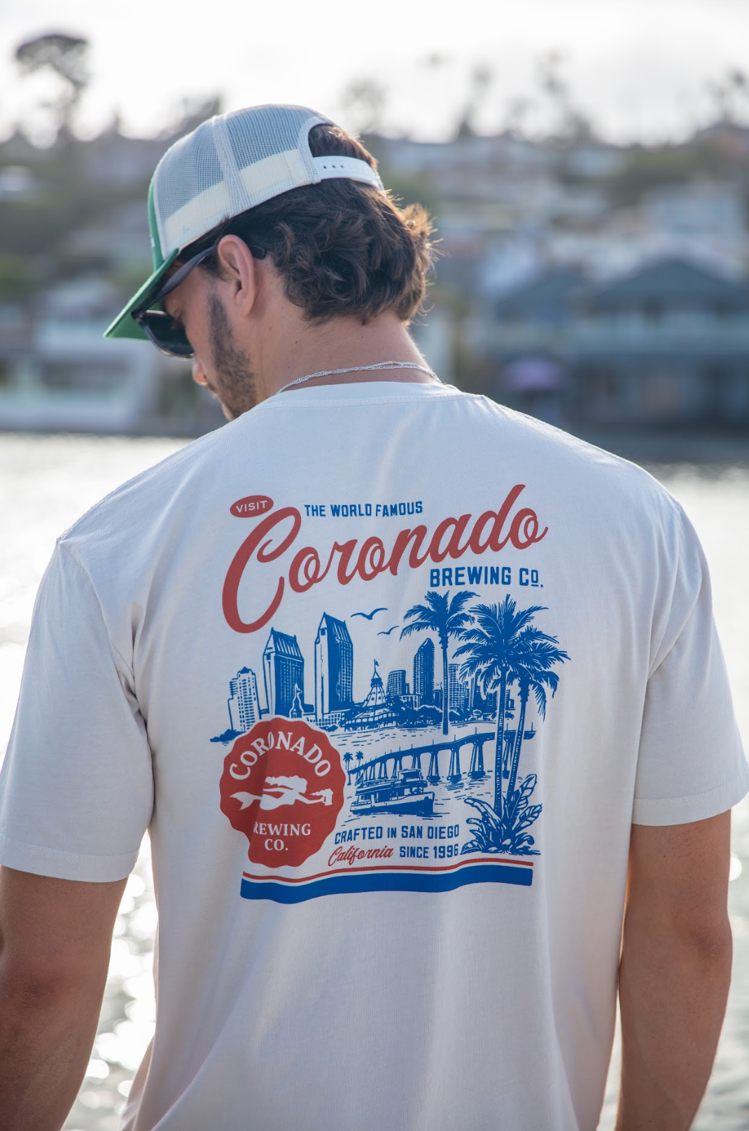 Person wearing a white t-shirt with Visit Coronado Brewing Co. graphic by a waterfront.
